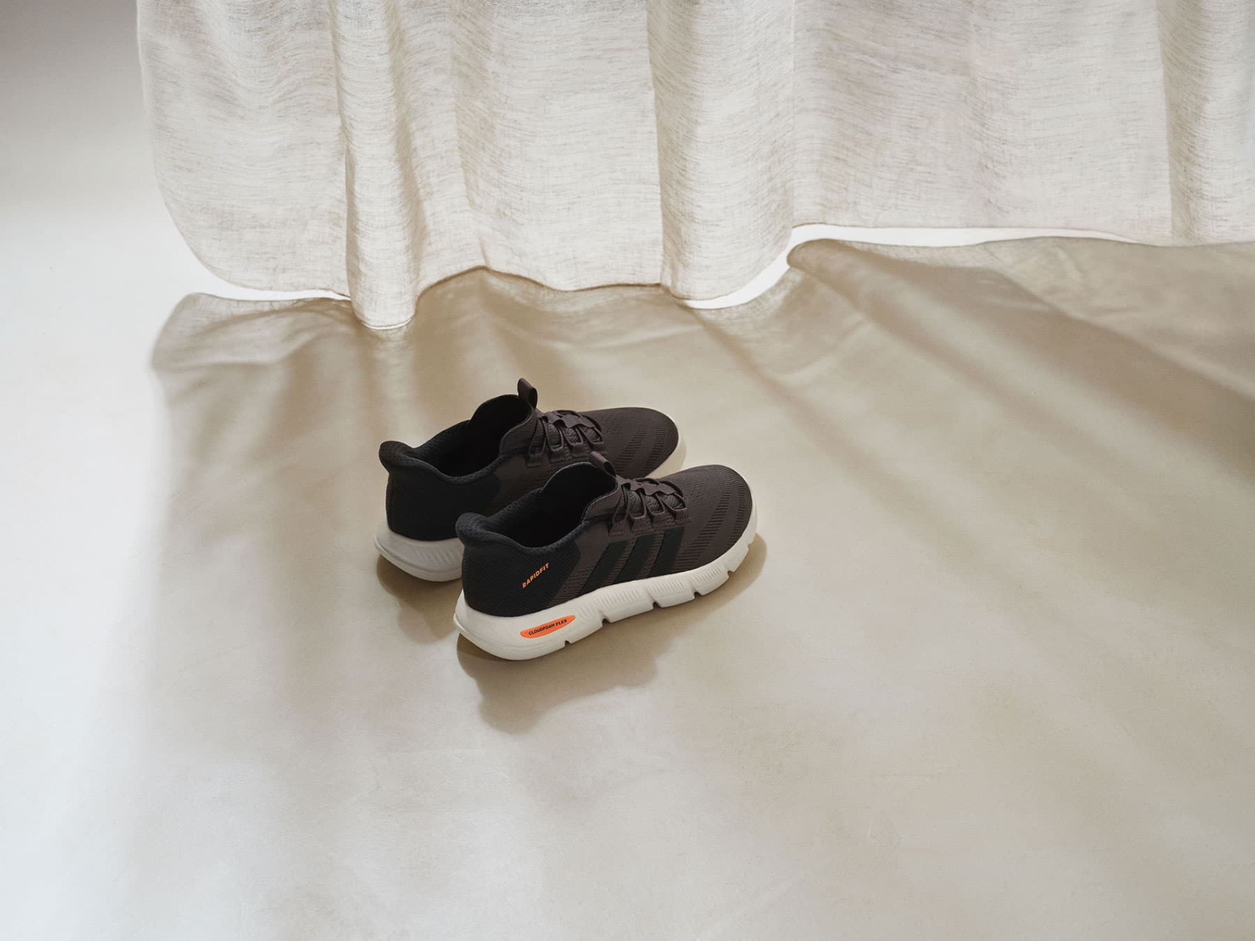 Graue adidas Cloudfoam-Sneaker stehen vor einem Vorhang.